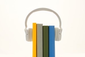 The image is of a set of headphones placed over 4 books, looking like the books may be listening to whatever is on the headphones.
